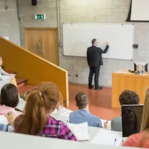 A group of people sitting in front of a white board.