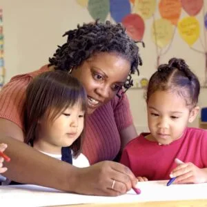 A woman and two girls drawing on paper.