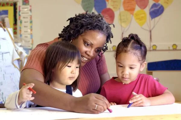 A woman and two girls drawing on paper.