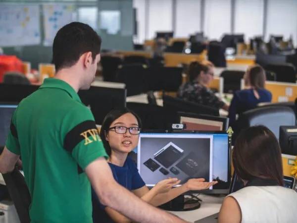 woman sitting in front of computer monitor explaining something two man and woman beside her