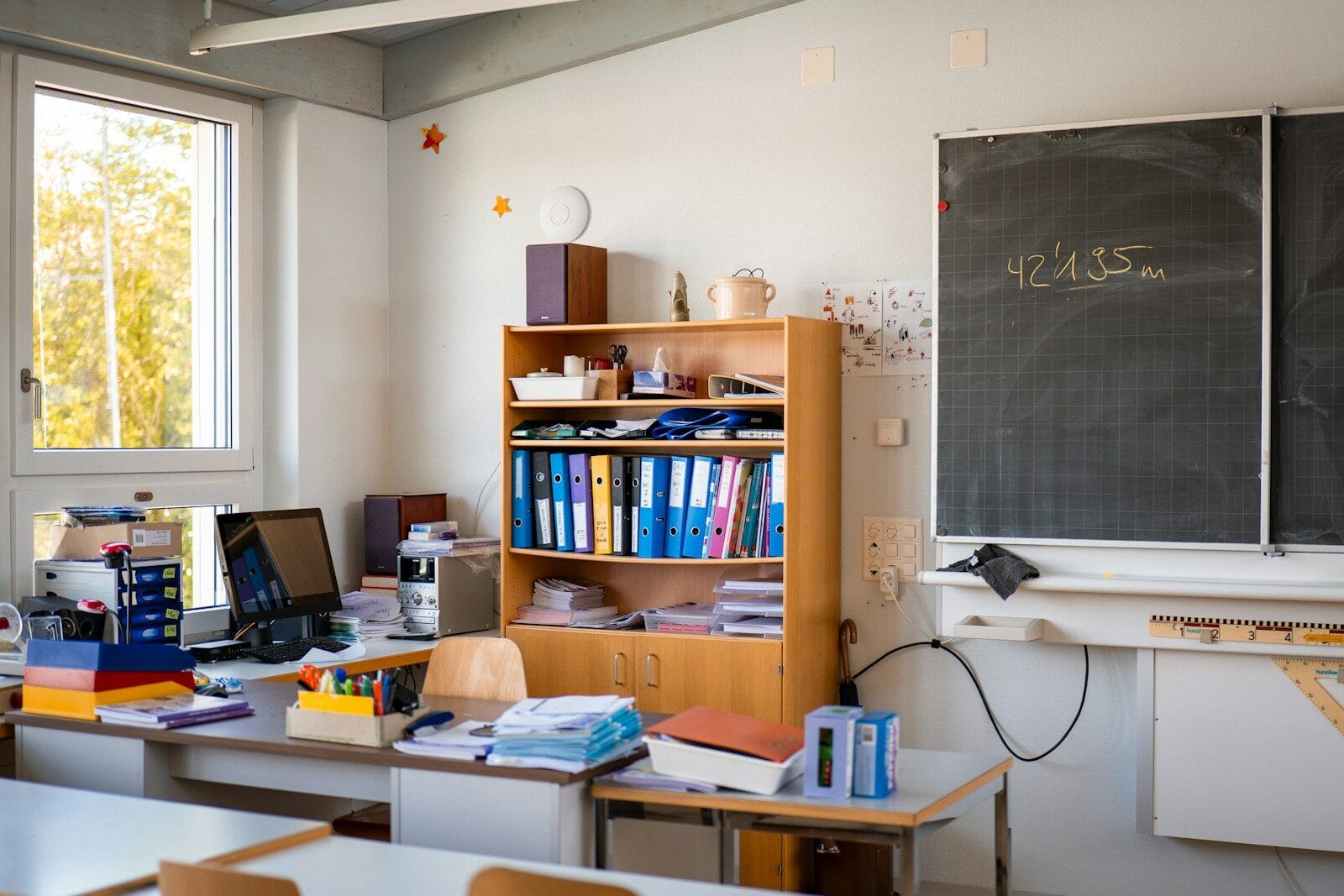 A classroom with supplies, desk, and a chalkboard.
